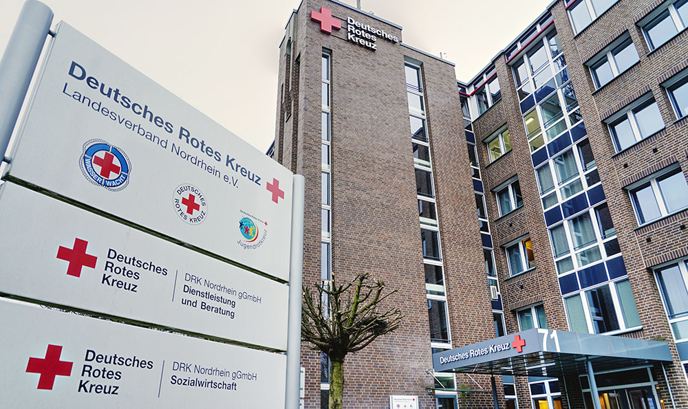 Frontansicht der DRK Nordrhein Akademie in Düsseldorf: mehrstöckiges Backsteingebäude mit rotem Kreuz und Schriftzug 'Deutsches Rotes Kreuz' über dem Haupteingang.
